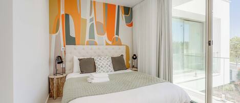 A modern bedroom with a large bed, a headboard with abstract art, two bedside lamps, and a view of the outdoors through a sliding glass door.