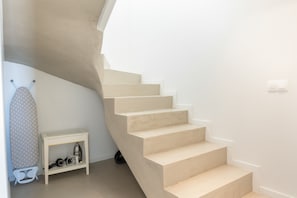 Eine Treppe mit einer hellen Wand, ein kleiner Tisch mit Bügelbrett und Kinderwagen, und ein weißer, an der Wand befestigter Lichtschalter.