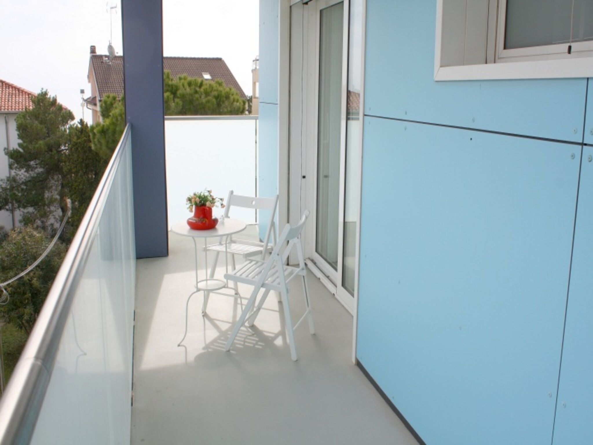 Un balcon avec des chaises blanches et une petite table, une plante en pot et une vue sur le quartier.