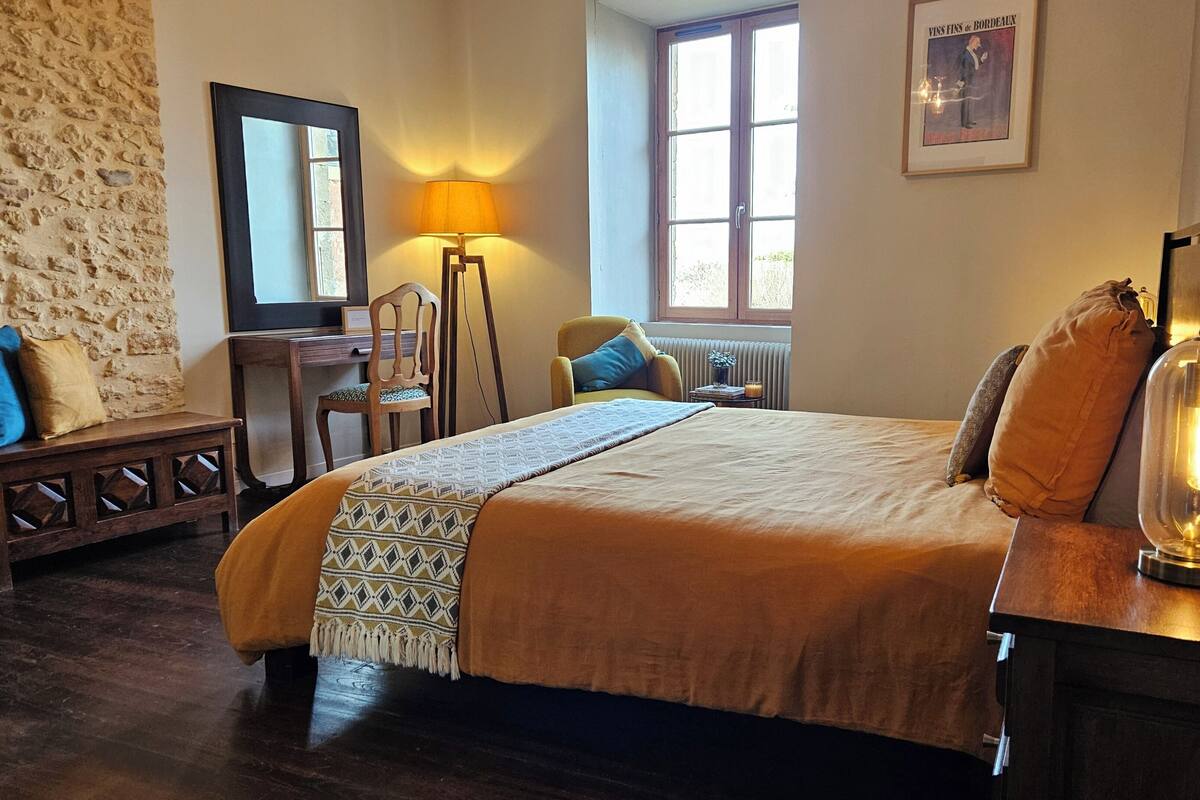 Een slaapkamer met een bed, een bureau, een stoel, een lamp en een raam.
