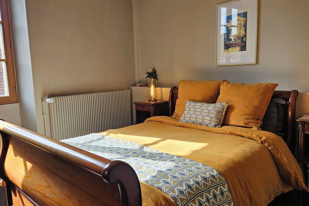 Een slaapkamer met een bed, nachtkastje, radiator, raam en een lijst met een kaart aan de muur.