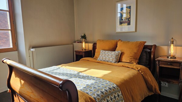 A bedroom with a bed, a nightstand, a radiator, a window, and a framed map on the wall.