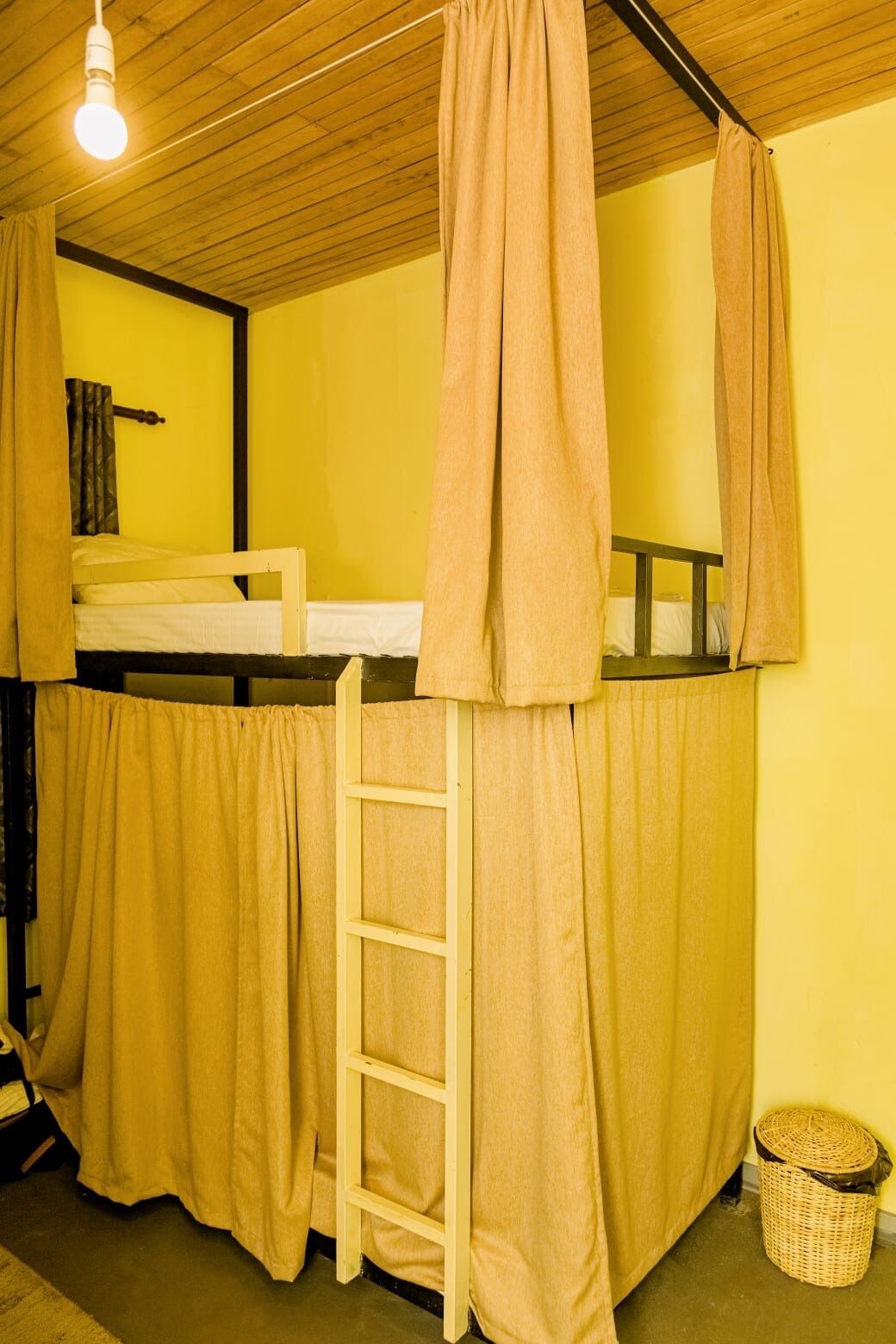 Een slaapkamer met een stapelbed, een ladder, een hanglamp en een rieten mand.
