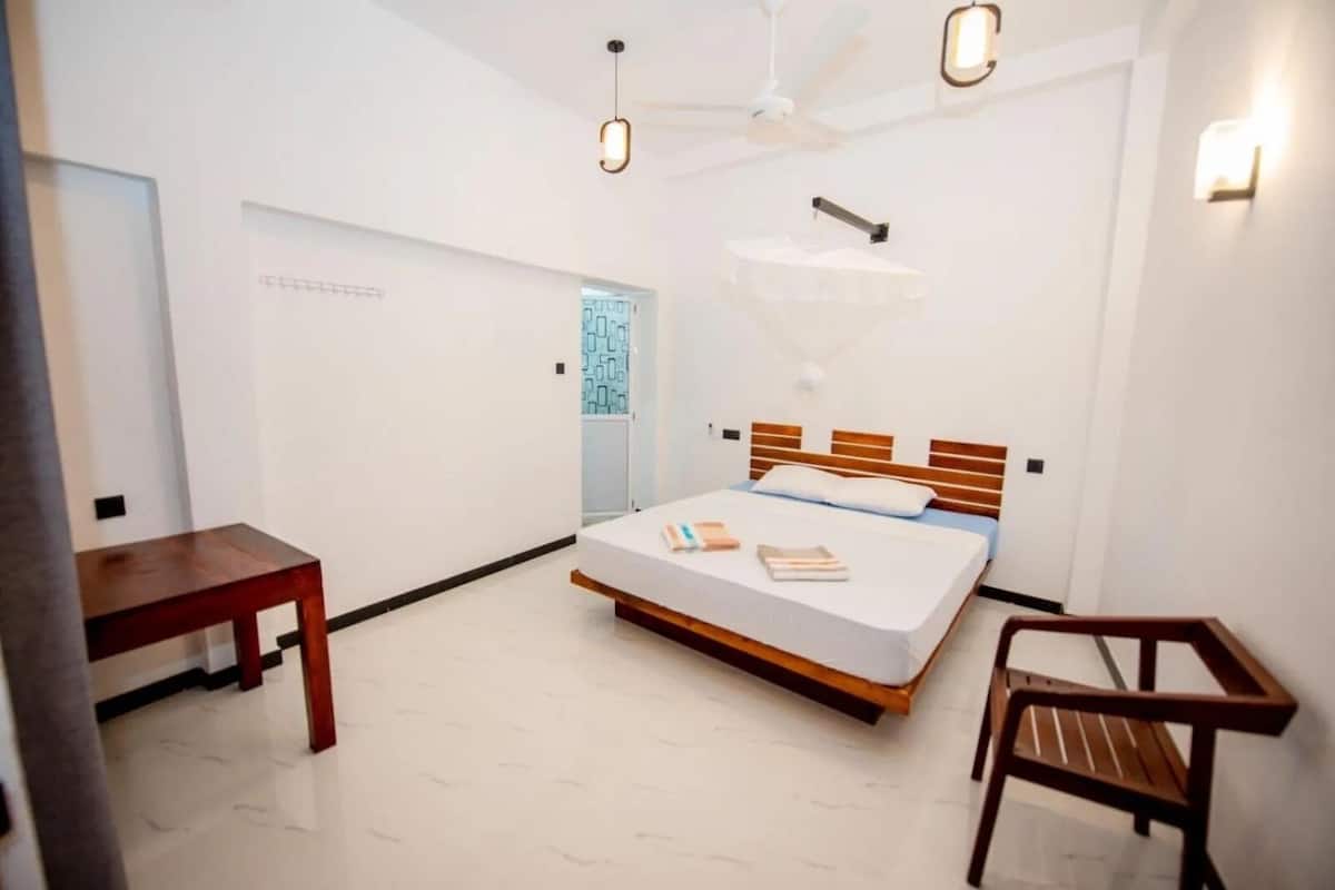 A modern bedroom with a bed, bedside table, chair, and a ceiling fan.