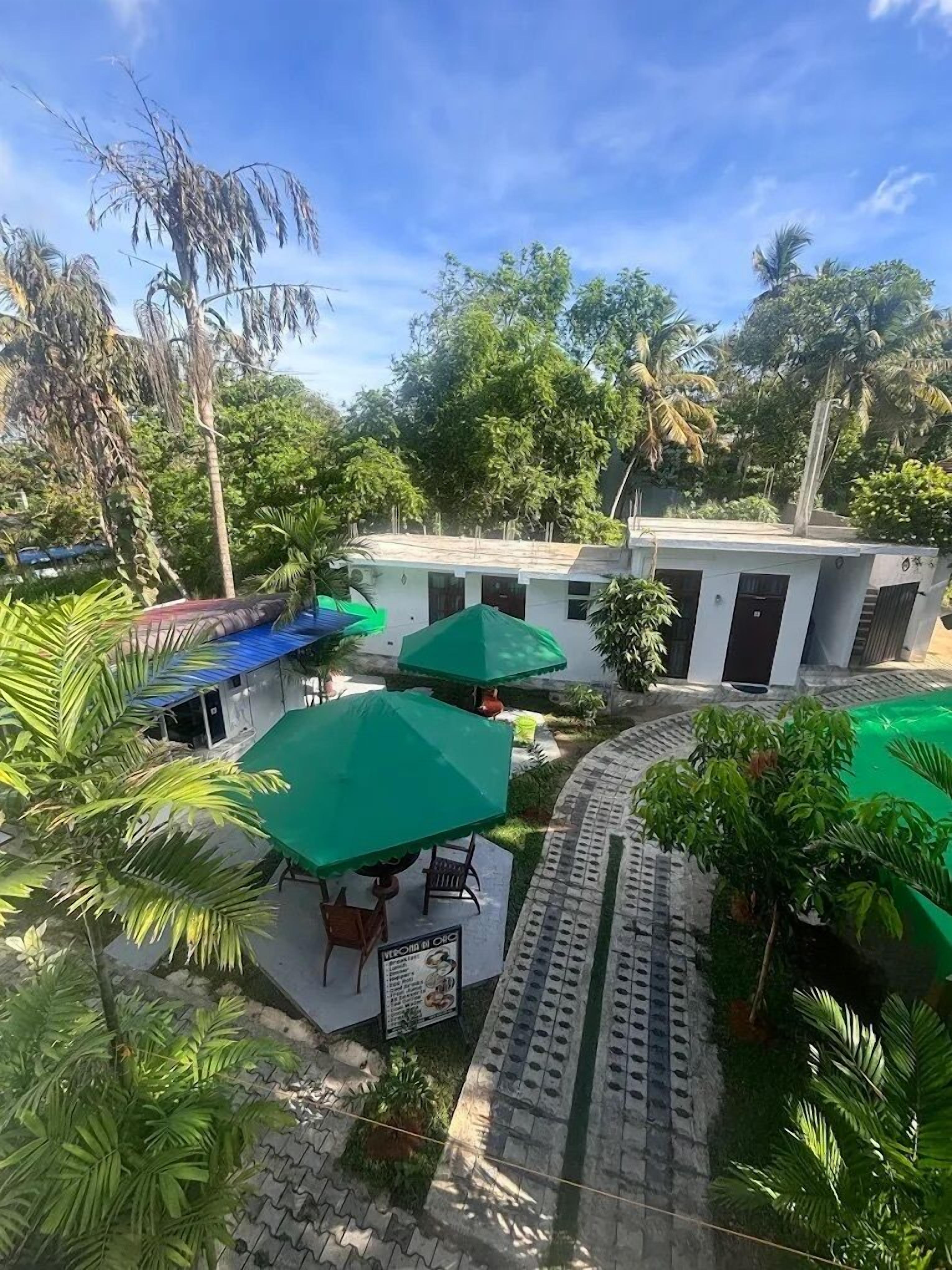 A courtyard with a building, green umbrellas, and palm trees.