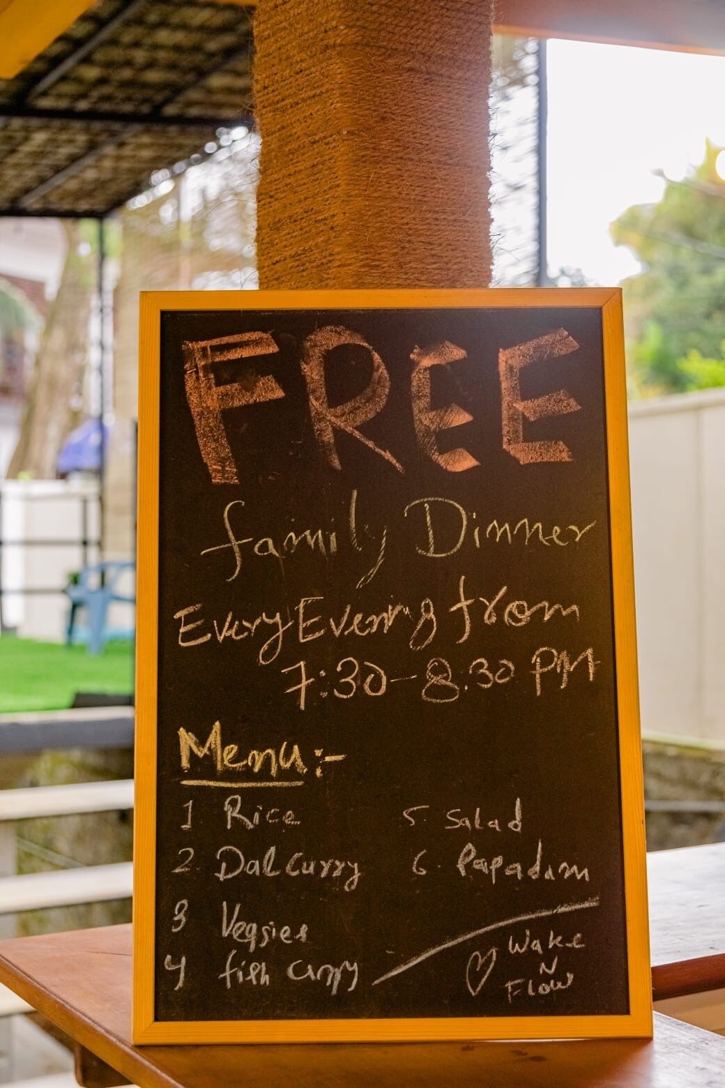 Quadro negro anunciando um jantar gratuito para a família, com menu que inclui arroz, salada, curry de dal, papadum, legumes e curry de peixe.