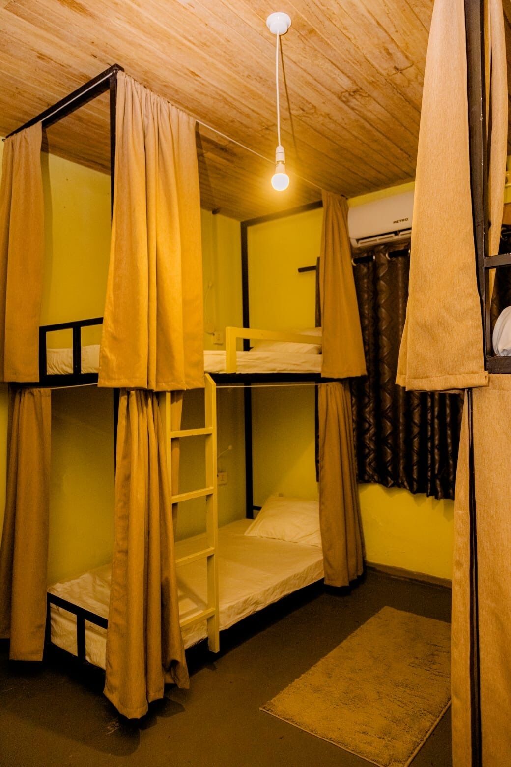 A bunk bed room with a ladder, a hanging light bulb, and a small rug.