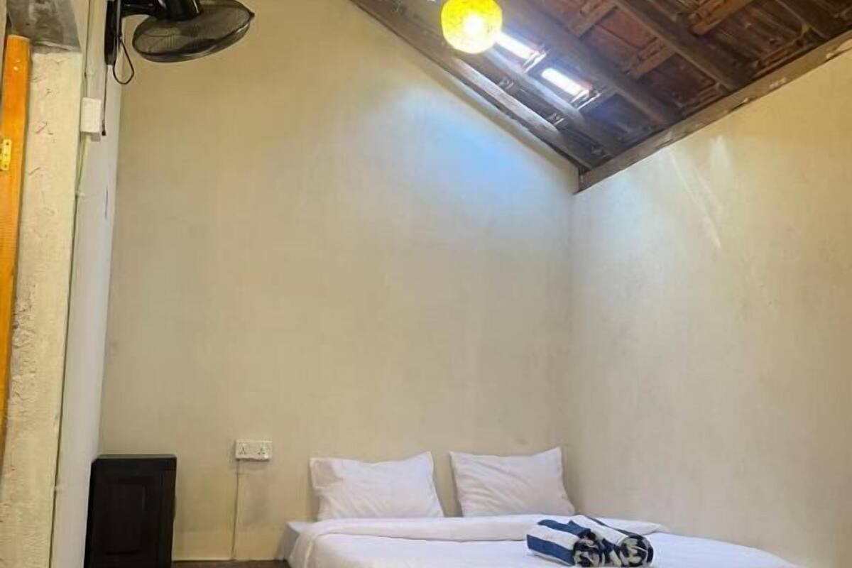 A small, single-bed room with a sloped ceiling and a hanging light fixture.