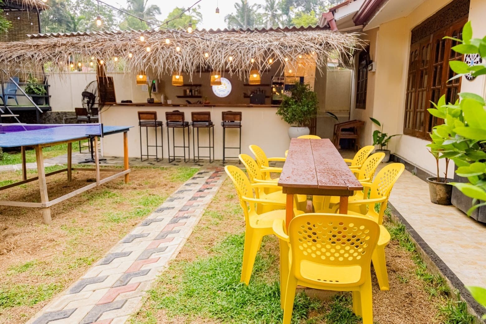 A patio area with a table and chairs, a thatched roof, and a wall-mounted grill.