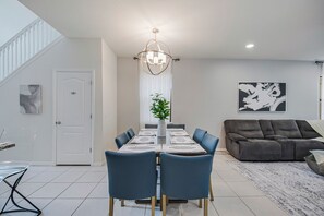 Et moderne spiseområde med et rektangulært bord, blå stole, en lysekrone og en grå sofa i baggrunden.