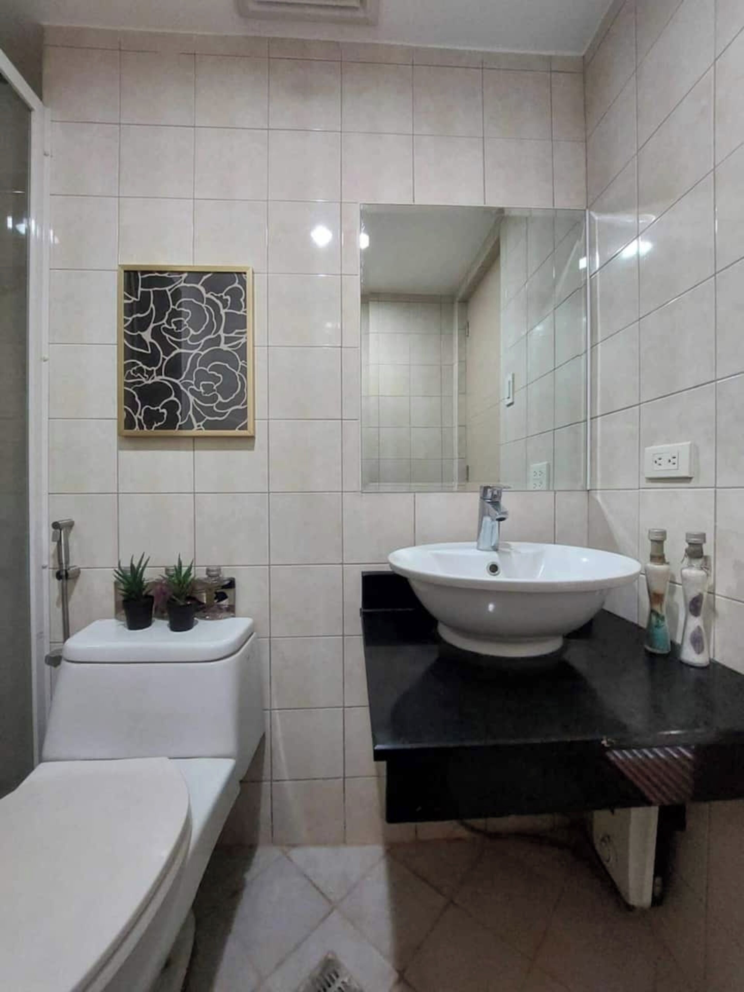 A bathroom with a toilet, sink, mirror, and decorative wall art.