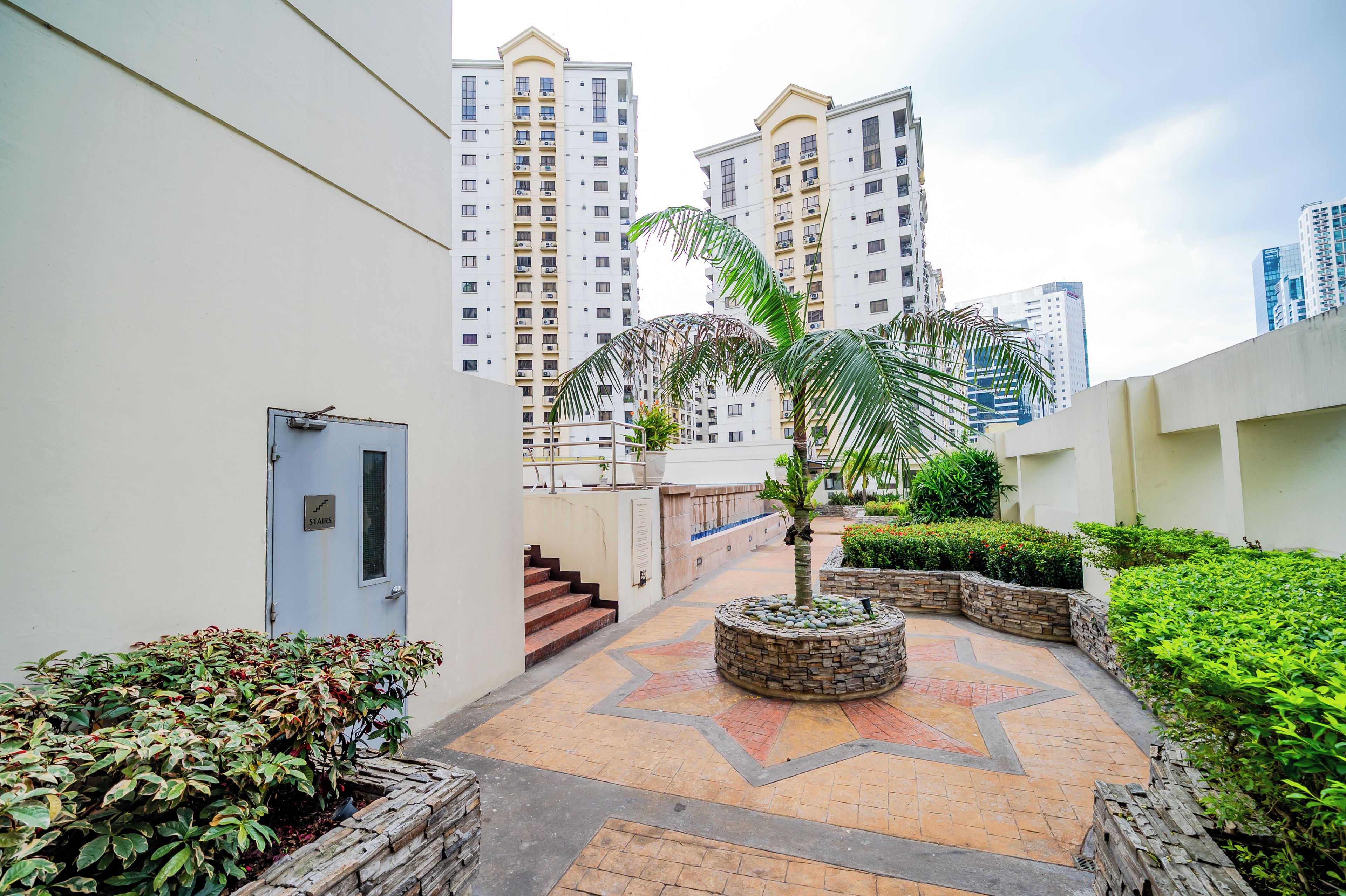 A courtyard with a palm tree, a staircase, and a building with multiple floors in the background.