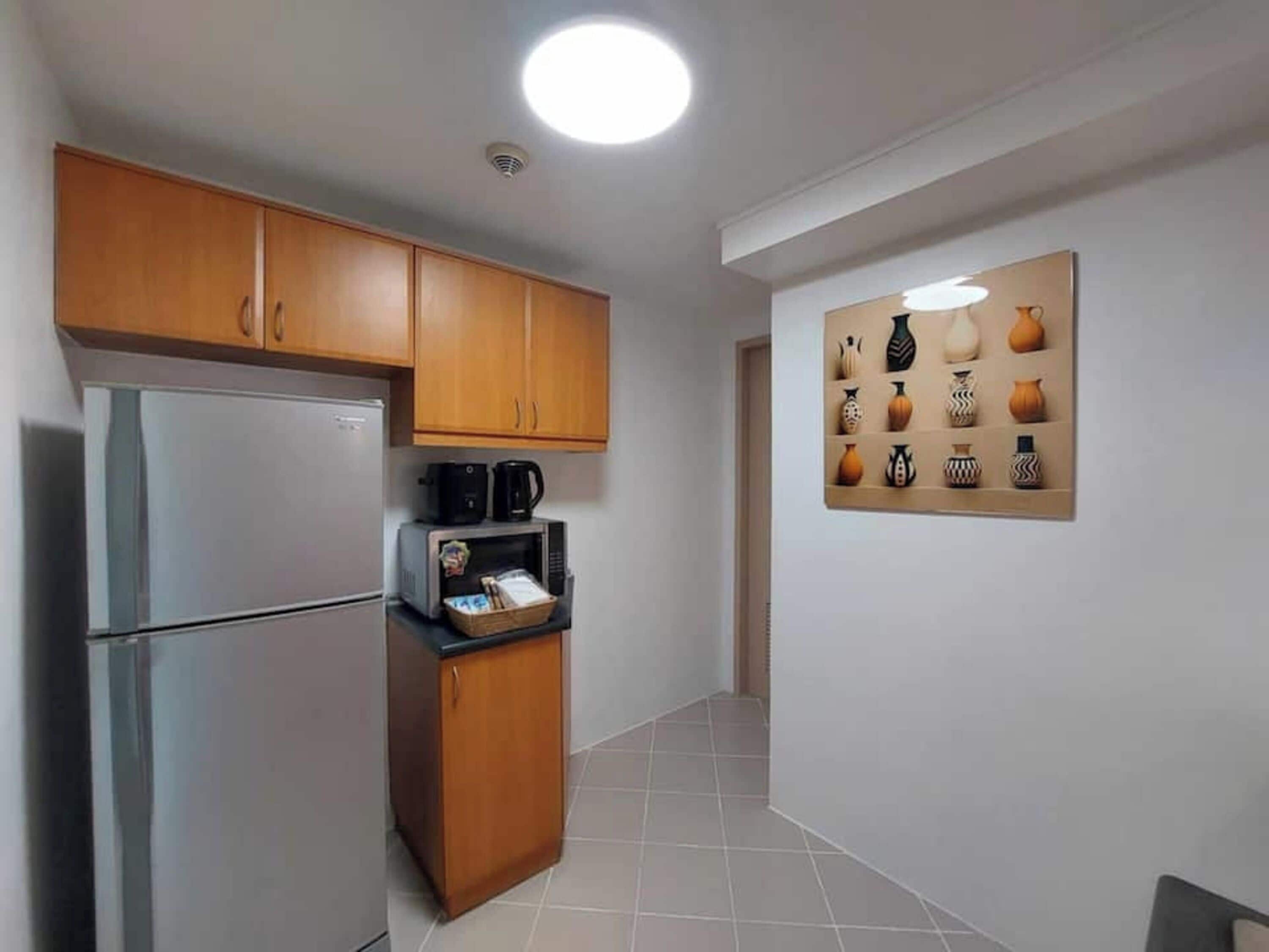 Une cuisine avec des meubles de rangement en bois, un réfrigérateur, un four à micro-ondes et une machine à café.