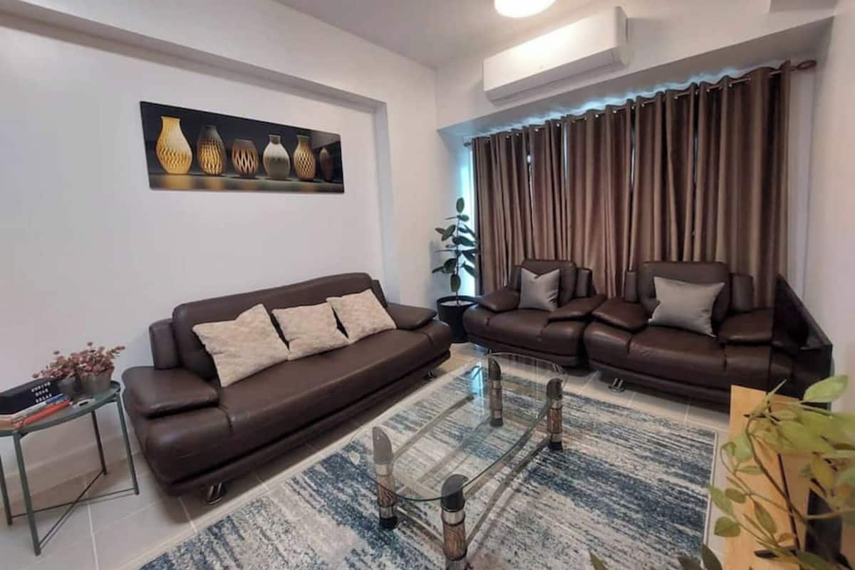 Una sala de estar moderna con un sofá marrón, una mesa de centro de vidrio y una alfombra estampada.