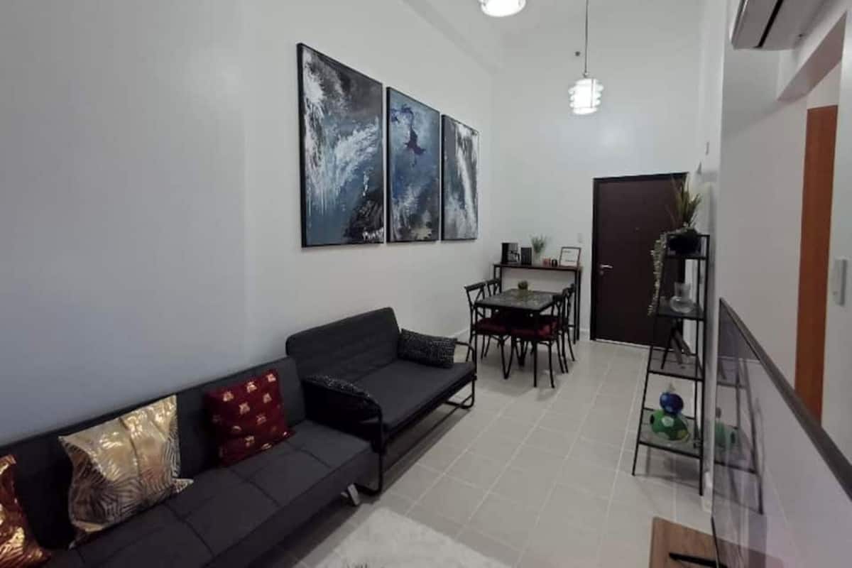 Una sala de estar moderna con un sofá, una mesa de comedor con sillas y dos obras de arte colgadas en la pared.