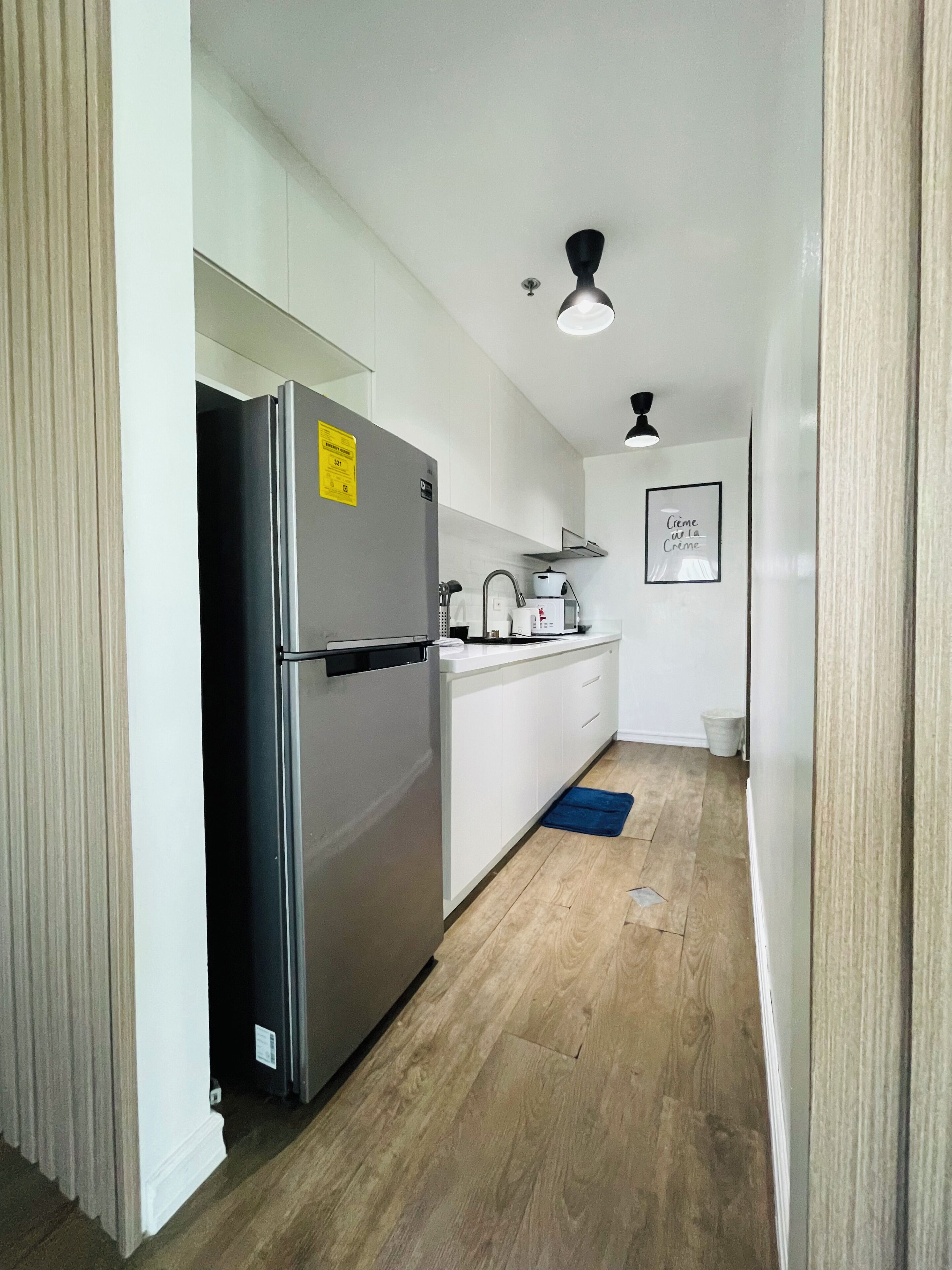 A compact kitchen with a stainless steel refrigerator, white cabinets, a microwave, and a ceiling fan.