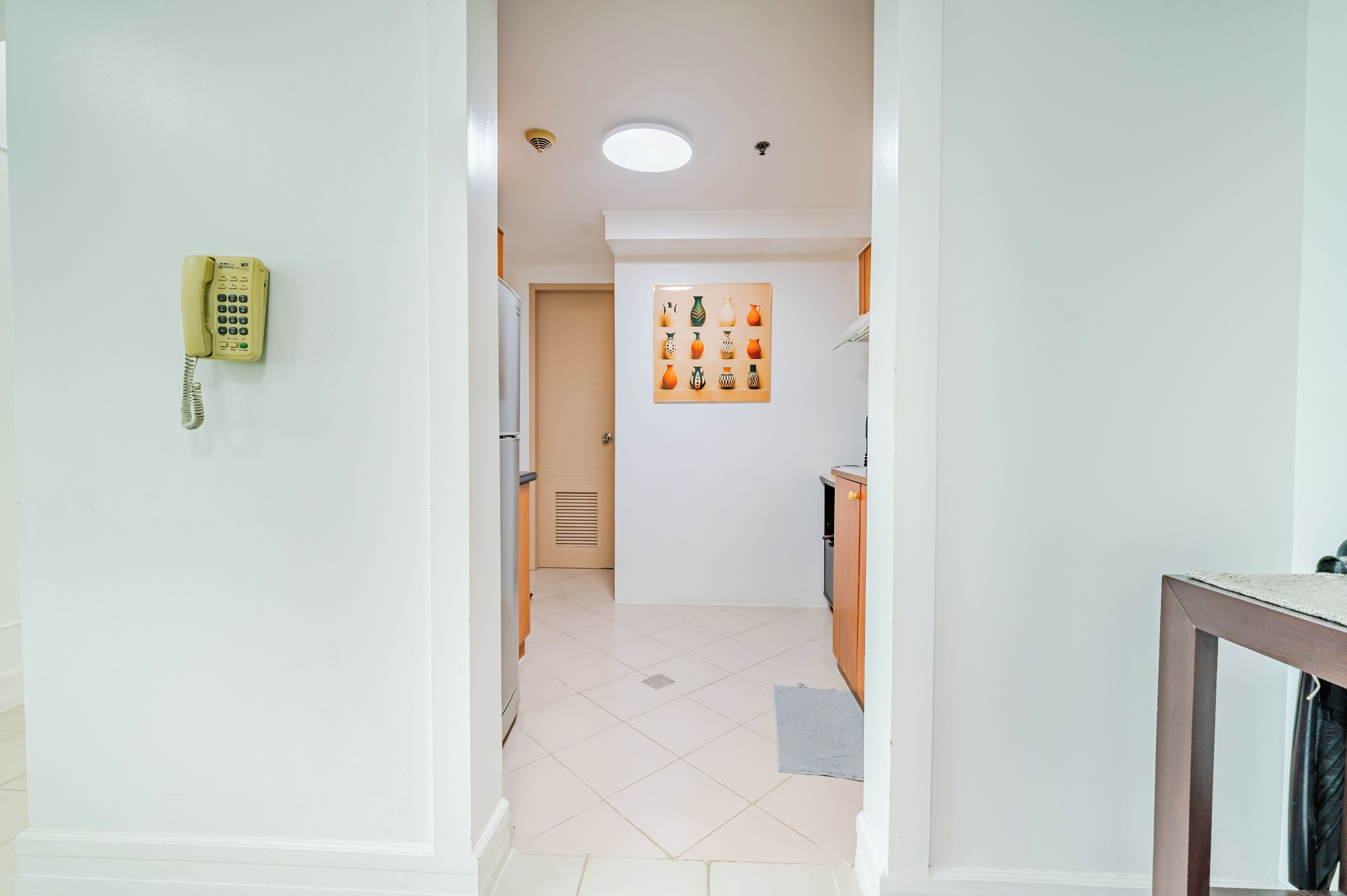 A hallway leading to a kitchen with a telephone, a door, and a wall-mounted vase collection.