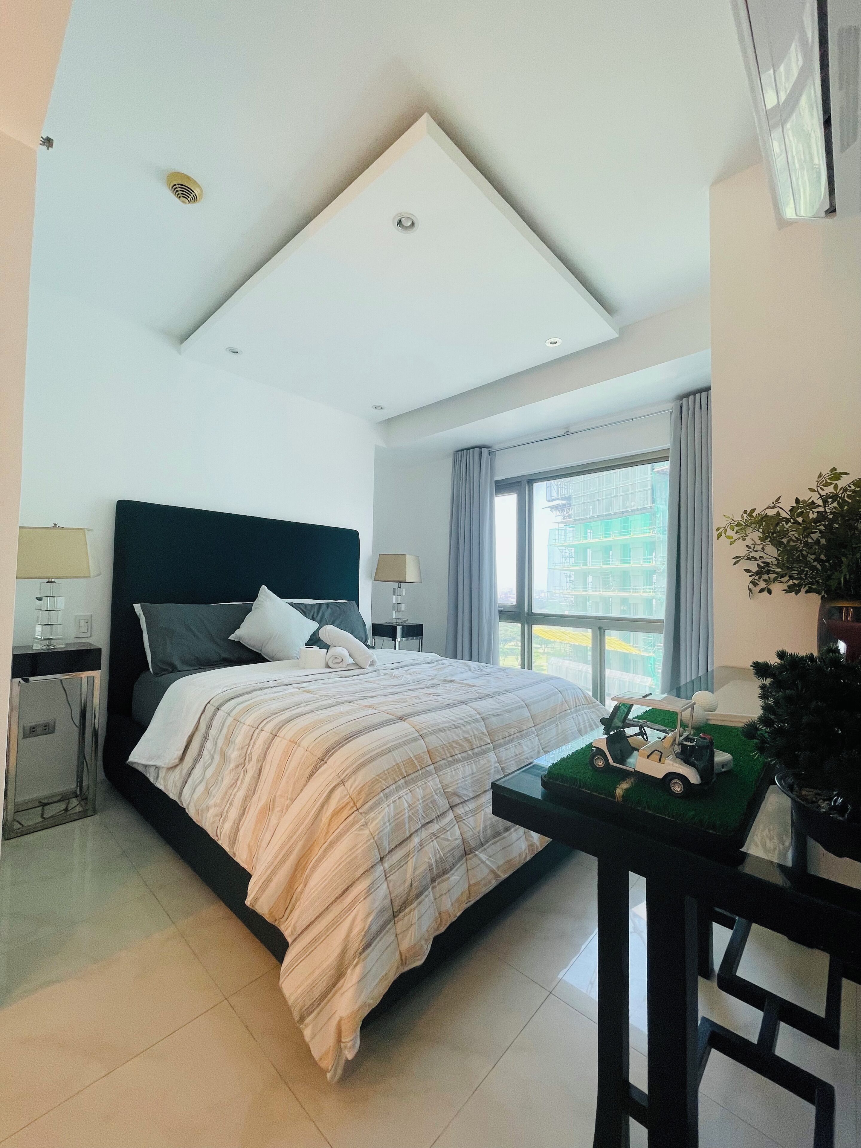 Habitación de hotel moderna con una cama grande, un escritorio, una planta en maceta y vistas a la ciudad.