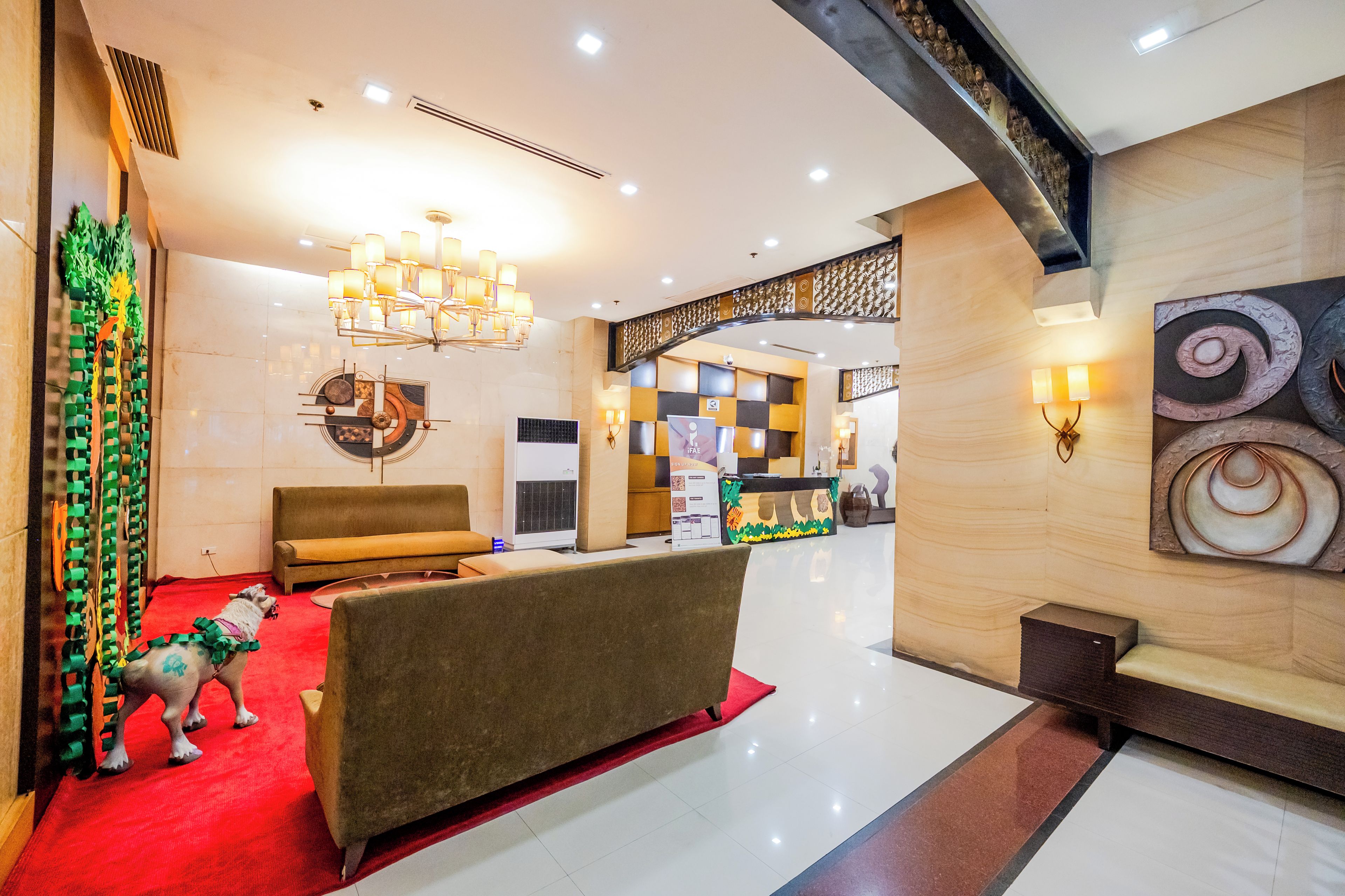 A hotel lobby with a reception desk, a sofa, a decorative wall, and a chandelier.