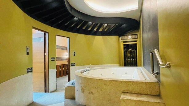 Un interior moderno con una escalera curva que lleva a un área de spa, incluyendo una bañera de hidromasaje y un banco de madera.
