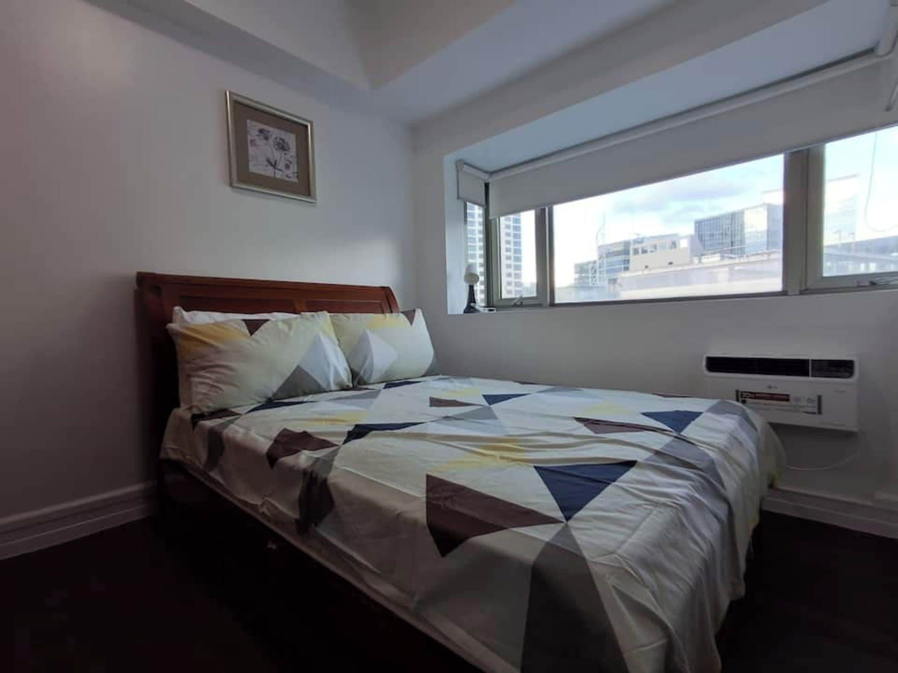 Un dormitorio con cama, ventana y aire acondicionado instalado en la pared.