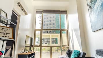 A modern living room with a sofa, a TV, a bookshelf, and a large window with a view of buildings.