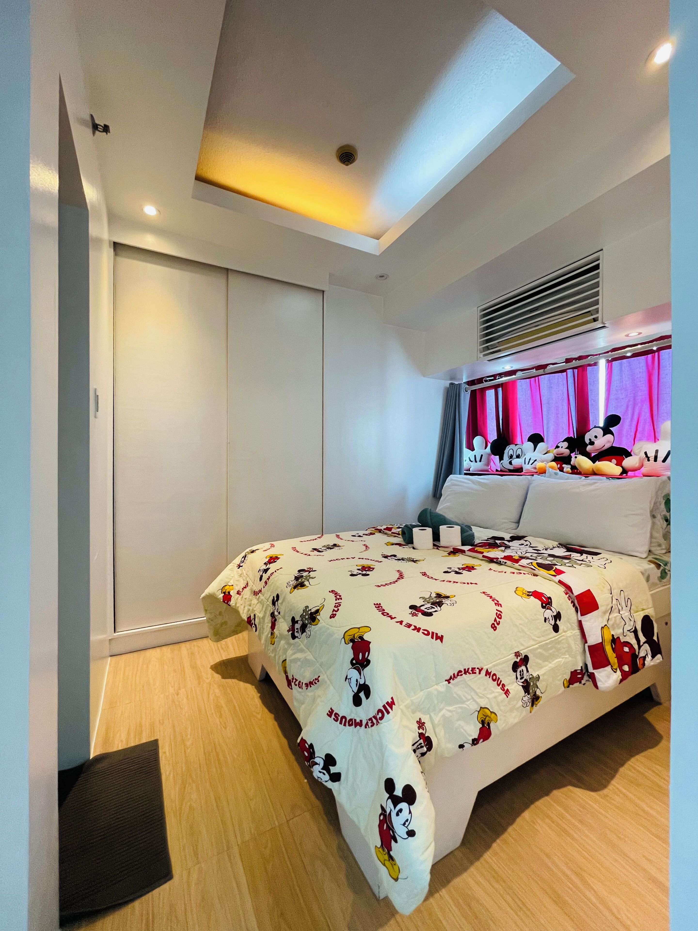 Un dormitorio con una colcha con temática de Mickey Mouse, un armario cerrado y una lámpara de techo.