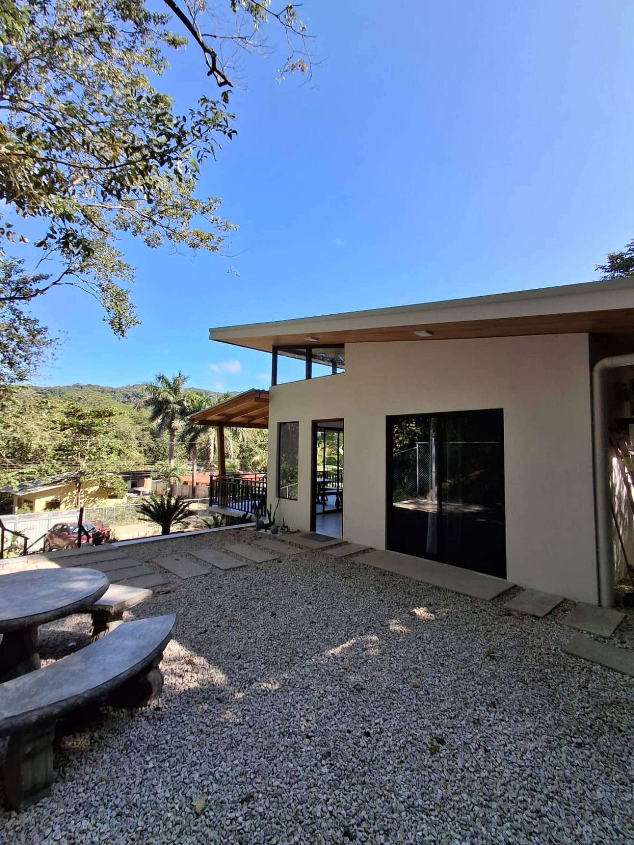 A modern house with a patio, a dining table, and a view of the surrounding landscape.