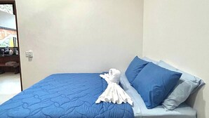 Un lit simple avec une couette bleue, une serviette blanche et une table de chevet en bois sur laquelle repose un livre.