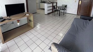 Ein Wohnzimmer mit einer Couch, einem Fernseher auf einem Holzboden und einer Küche im Hintergrund.