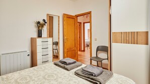 A bedroom with a bed, a dresser, a chair, and a wooden door. - Casa Emilia: Rural Retreat with Private Terrace, Garden, and Wi-Fi (Baeza)