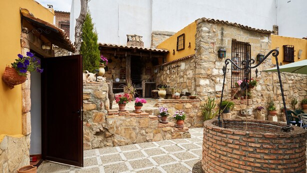 A courtyard with a brick well, terracotta pots with flowers, and stone walls. - Casa Emilia: Rural Retreat with Private Terrace, Garden, and Wi-Fi (Baeza)