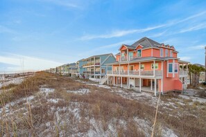 A beachfront property with multiple houses, a sandy beach, and a clear sky. - Victorian Style Beachfront Home Perfect Family Vacation Destination (Gulf Shores)