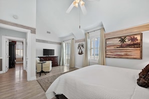 A hotel room with a bed, a TV, a desk, and a painting on the wall. - Victorian Style Beachfront Home Perfect Family Vacation Destination (Gulf Shores)