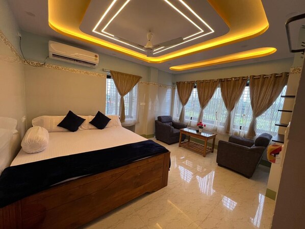 A hotel room with a large bed, a seating area with a sofa and armchairs, and a ceiling with modern lighting.