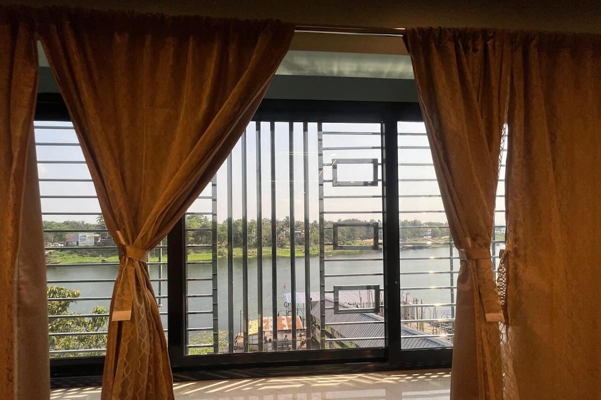 A room with a large window overlooking a body of water, a balcony, and a view of a bridge.