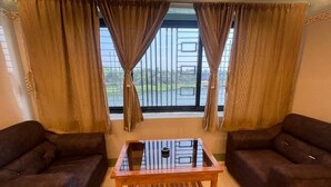 Una habitación con dos sofás, una mesa de vidrio y vistas a través de una ventana con cortinas.