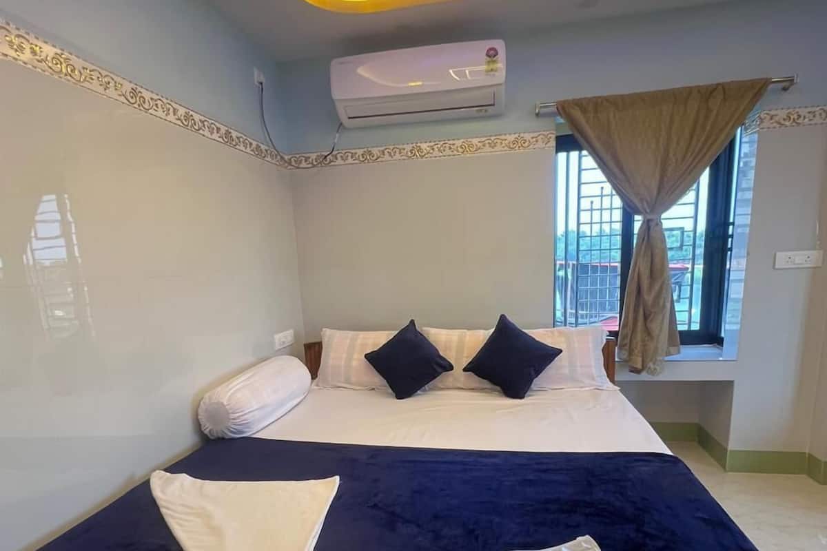 A bedroom with a bed, air conditioning unit, window with curtains, and a view of the outside.