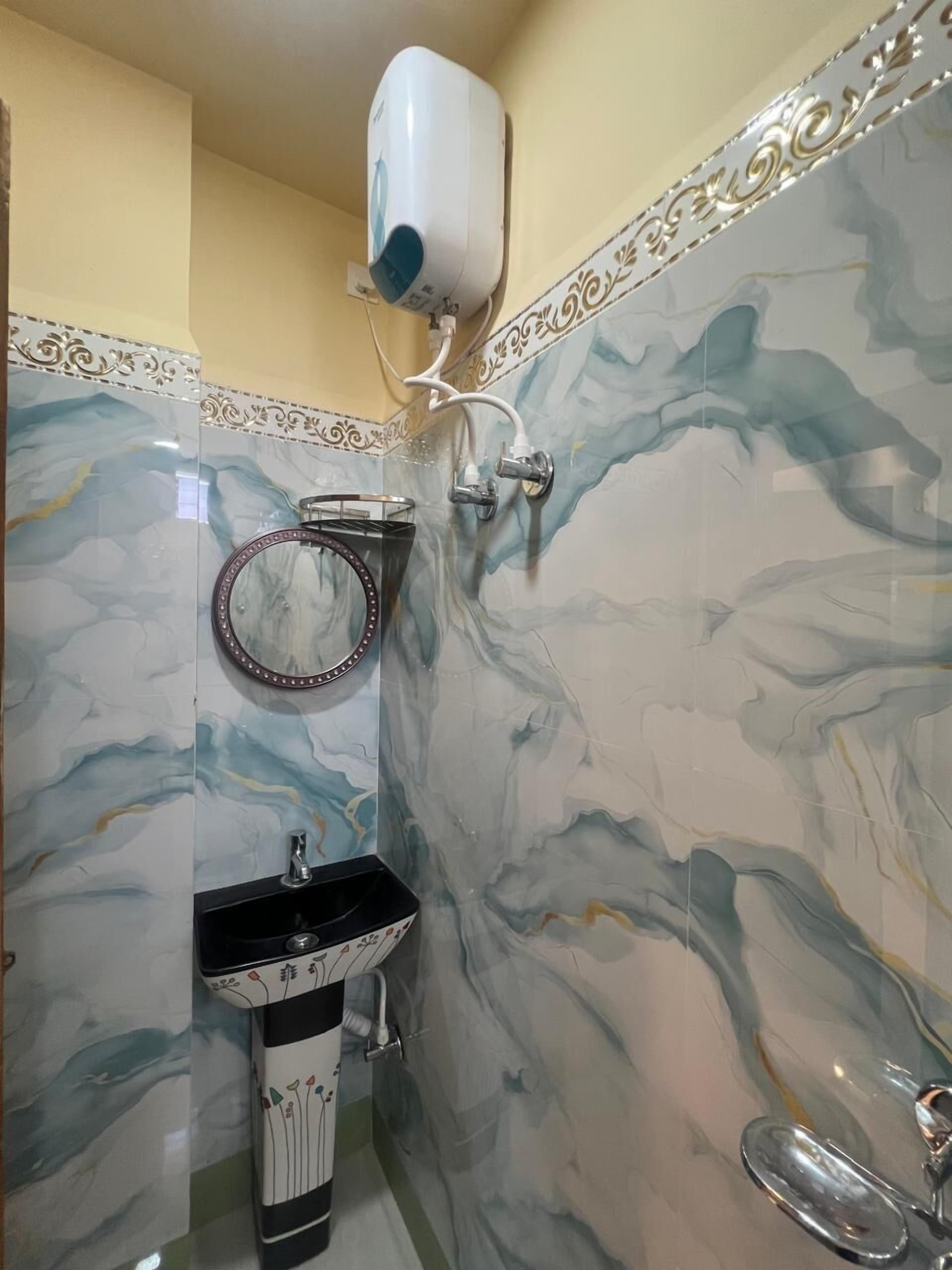 Un baño con pared de mármol, un lavabo con una pila decorativa, un espejo con marco ornamental y un secamanos fijado a la pared.