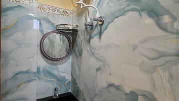 Un baño con pared de mármol, un lavabo con una pila decorativa, un espejo con marco ornamental y un secamanos fijado a la pared.