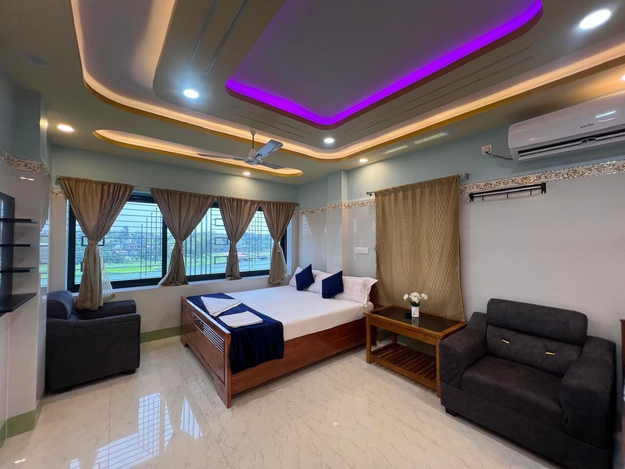 Una habitación de hotel moderna con cama, sofá, mesita de noche y ventilador de techo.