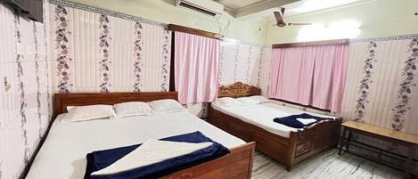 A bedroom with two wooden beds, a bench, a ceiling fan, an air conditioner, and patterned wallpaper.