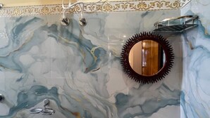 Un baño con pared de mármol, un lavamanos, un espejo, un secador de pelo y un cabezal de ducha.