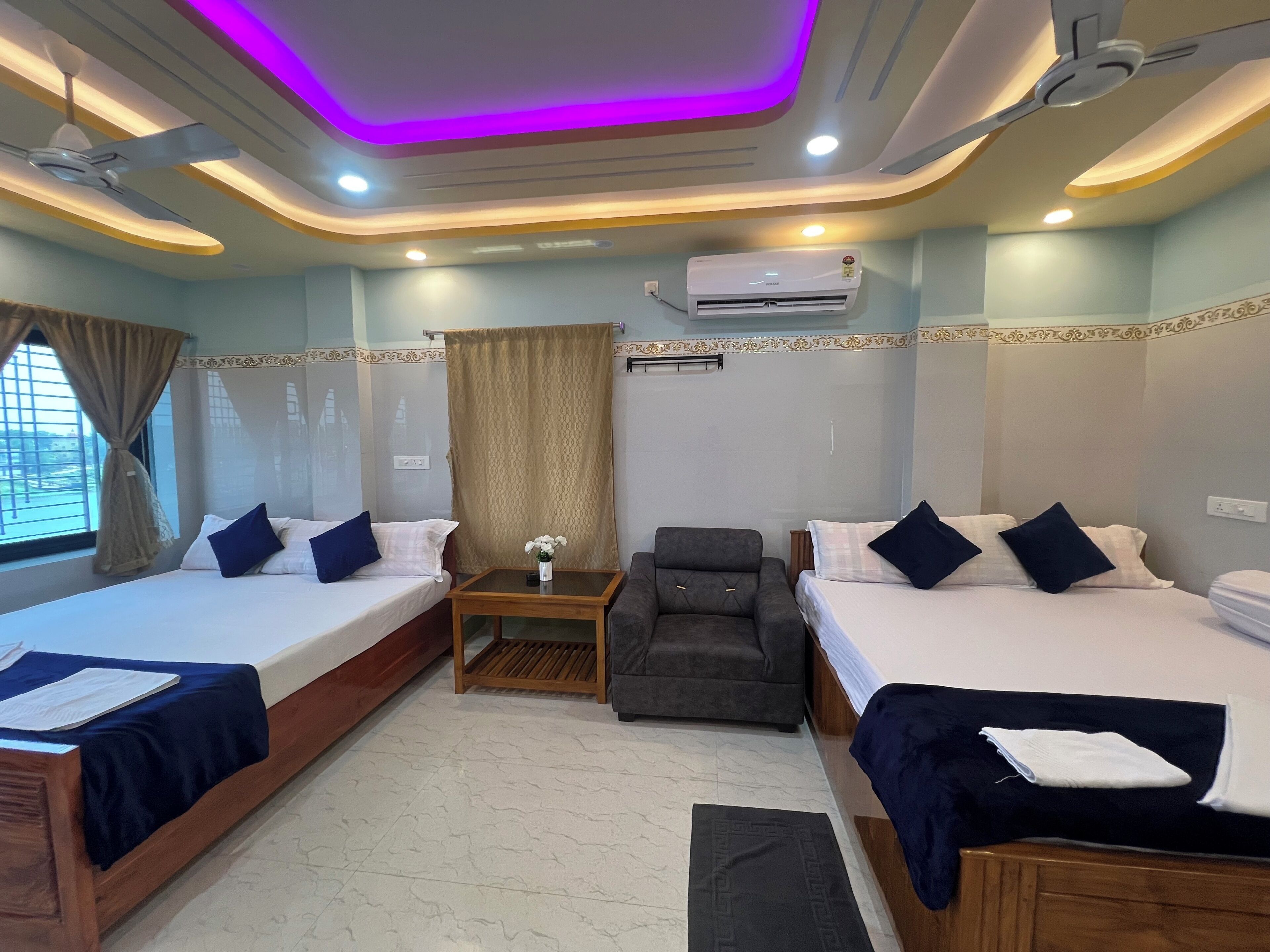 A hotel room with two beds, a desk, a chair, an air conditioner, and a window with curtains.