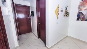 Um corredor com duas portas de madeira, um telefone fixado na parede, um letreiro de boas-vindas e um objeto decorativo na parede.