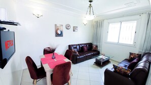 Uma sala de estar com televisão, sofá, mesa de centro e mesa de jantar.