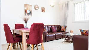 Uma área de refeições com mesa de madeira e cadeiras vermelhas, um sofá de couro marrom e uma pequena mesa lateral com um vaso.
