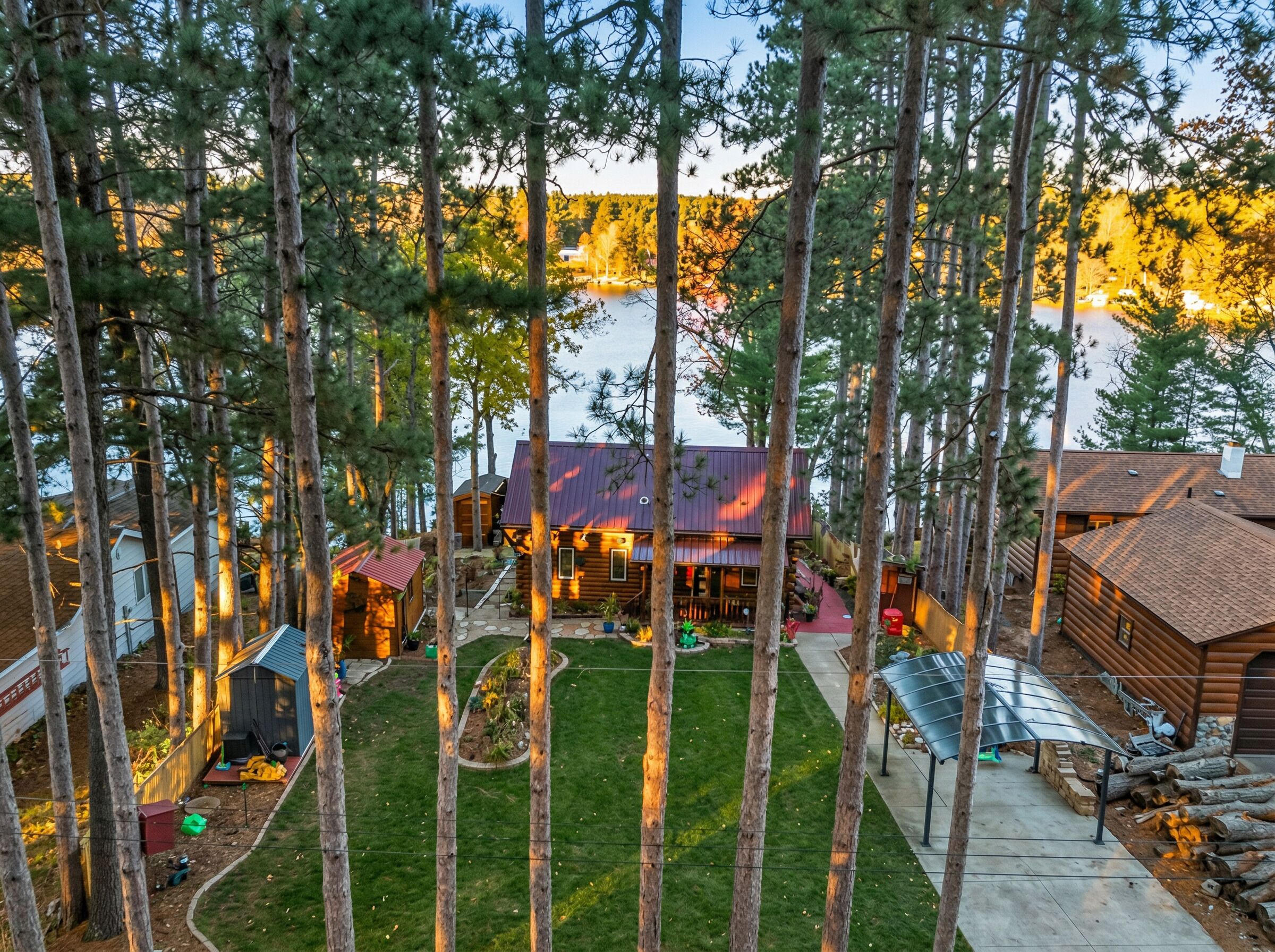A cabin with a metal roof, surrounded by tall trees and a small lawn.