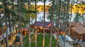 Une cabane avec un toit en métal, entourée de grands arbres et d’une petite pelouse.