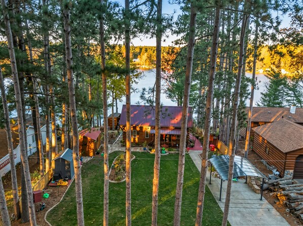 A cabin with a metal roof, surrounded by tall trees and a small lawn. - Bigfoot Lakefront Lodge: Fish. Hunt. Relax. Repeat. - 600 Public Acres Next Door (Oxford)
